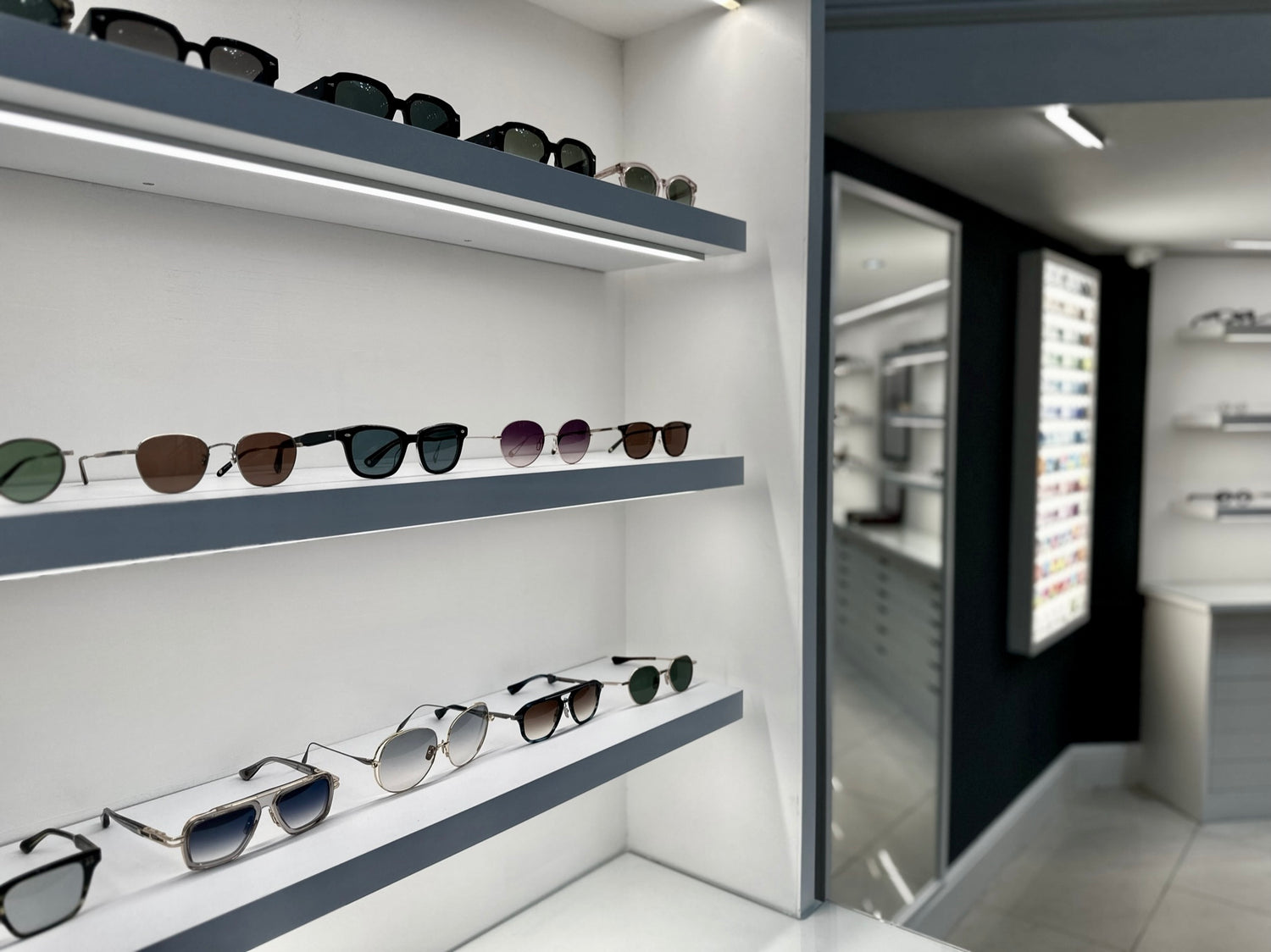 A picture of the Dickens Heath Practice in dramatic cool colours, showing a selection of Ahlem, Garrett Leight and Dita sunglasses and with the wall of tints (coloured lenses) in the background.
